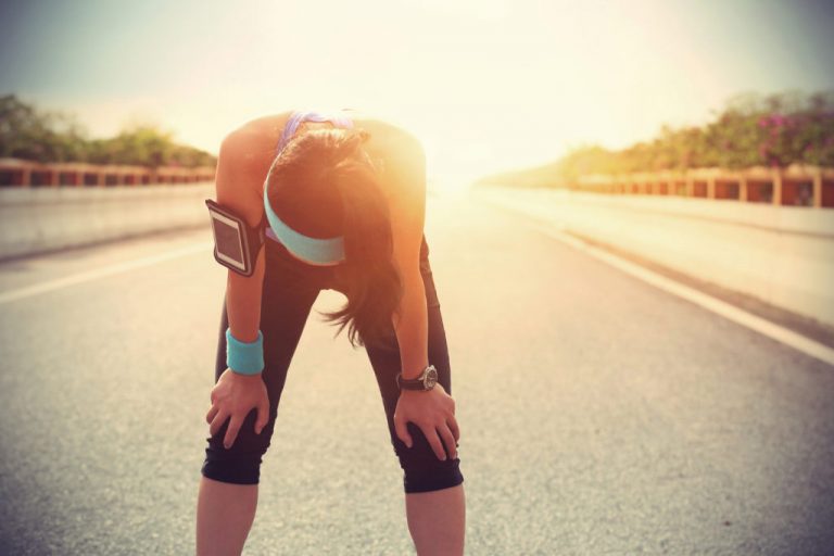 Exhausted female runner taking a break on a city street, leaning over with hands on knees.