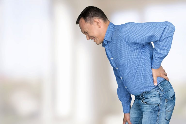 Individual experiencing a sciatica flare-up, holding their lower back in discomfort.